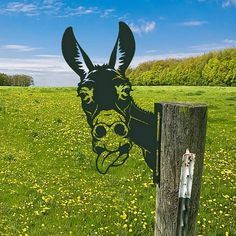 an animal head cut out of the side of a fence post in a field with dandelions