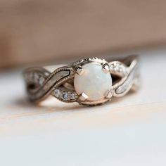 a white opal and diamond ring sitting on top of a table