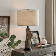 a wooden table with a lamp on top of it next to a plant and framed pictures