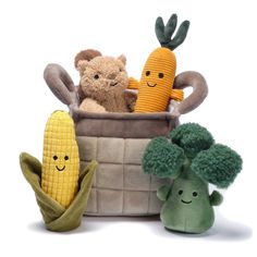 three stuffed animals sitting in a basket with corn on the cob and carrots