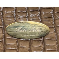 a close up view of the logo on an alligator skin leather bag with gold lettering