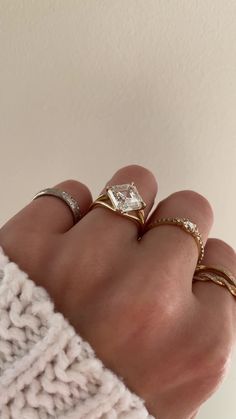 a woman's hand with three different rings on it and one is wearing a sweater