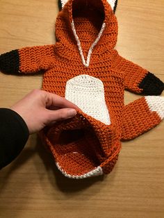 a person is holding an orange and white knitted fox hoodie on a table