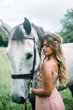 a woman in a pink dress standing next to a white horse with braids on it's head