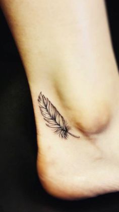 a small feather tattoo on the side of a woman's foot with a black and white design