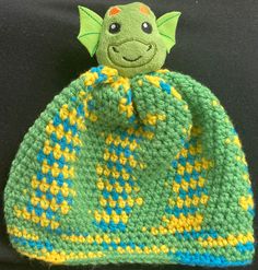 a green crocheted hat with a yellow and blue design on the front, sitting on a black surface