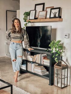 a woman standing in front of a tv on top of a wooden shelf next to a plant