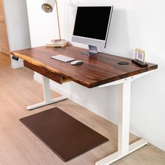 a wooden desk with a computer monitor and keyboard on it in front of a white wall