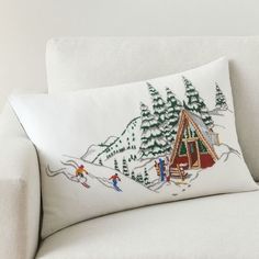 a white couch with a christmas pillow on it's back and a small cabin in the background