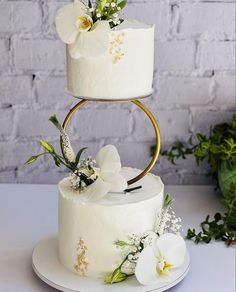 three tiered cake with white flowers and greenery on the top, against a brick wall