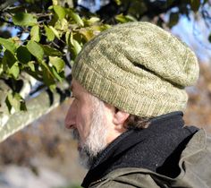 an older man wearing a green knitted hat looking at something in the distance while standing next to a tree