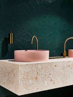 two pink sinks sitting next to each other on top of a black counter in front of a green wall