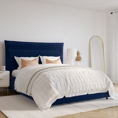 a white bed with blue headboard in a bedroom next to a window and lamp