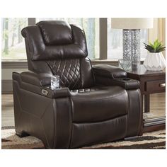 a brown recliner chair sitting on top of a rug next to a table and lamp