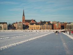 people are walking in the snow near buildings and a large body of water that has been frozen over