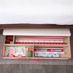 an open suitcase filled with wrapping paper on top of a wooden floor next to a bed