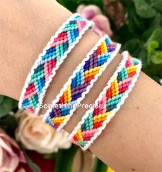 three bracelets with different colors and designs on each one hand, in front of flowers