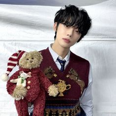 a young man holding two teddy bears wearing sweaters and ties, standing in front of a white backdrop