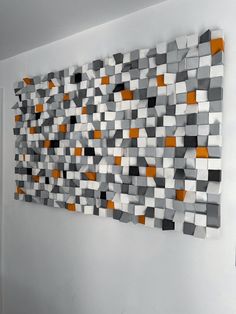 a wall sculpture made out of squares in grey and orange colors on a white wall