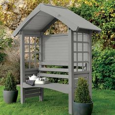 a gray wooden bench sitting on top of a green grass covered field next to potted plants