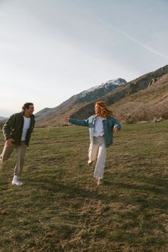 a man and woman are playing frisbee in a field with mountains in the background