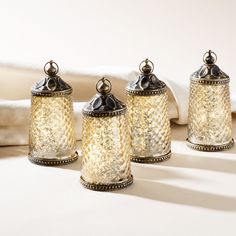 three glass jars sitting next to each other on top of a white tablecloth covered bed