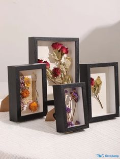 three black frames with flowers in them on a white tableclothed surface, one is holding a piece of paper and the other two are empty