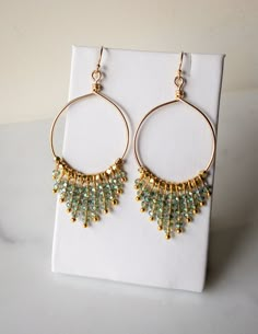 a pair of gold hoop earrings with blue and green beads on top of a white napkin