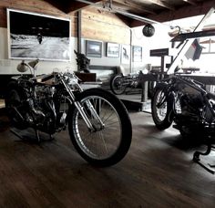 two motorcycles are parked in a room with wood flooring and wooden walls, along with pictures on the wall