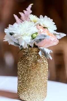 a vase filled with white and pink flowers on top of a table covered in gold glitter