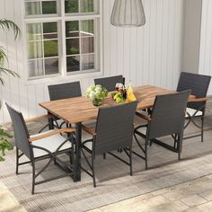 an outdoor dining table and chairs set up in front of a white house with potted plants