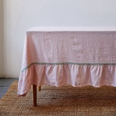 a pink tablecloth with green trim on top sitting on a rug in front of a white wall