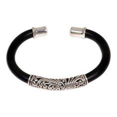 Sterling textures find bold contrast on a bracelet of black rubber. Crafted by hand a silver cylinder centers this cuff. Wayan Asmana's design is engraved with frangipani blossoms worn by Balinese men and women. .925 Sterling silver Elegant Adjustable Carved Bangle, Elegant Black Bracelet With Oxidized Finish, Elegant Carved Cuff Bracelet, Elegant Carved Adjustable Bracelet, Elegant Adjustable Carved Bracelet, Elegant Carved Bracelet, Sterling Silver Cuff Bracelet, Sterling Silver Cuff, Silver Cuff Bracelet