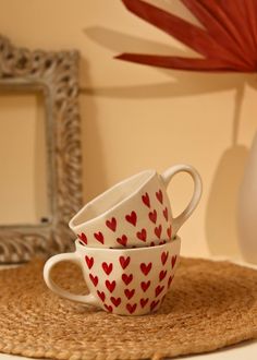 two coffee cups with hearts painted on them sit on a place mat in front of a mirror