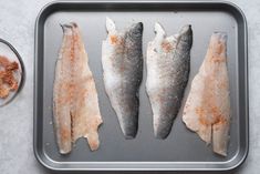 three fish are on a tray with seasoning next to it, and one is cut in half