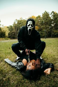 a person in a mask holding a knife over another person's head on the ground