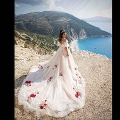 a woman in a wedding dress standing on top of a cliff overlooking the ocean and mountains