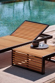 a wooden lounge chair next to a pool with a bowl on it's side