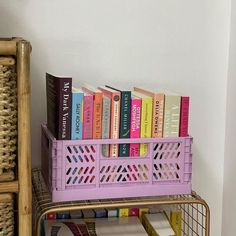 some books are sitting on a shelf next to a metal basket filled with colorful books