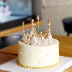 a white cake with gold decorations on top and two candles in the middle, sitting on a table next to a television