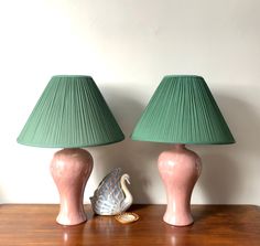 two pink lamps sitting on top of a wooden table next to a green lamp shade