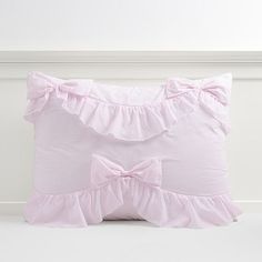 a pink pillow with ruffled edges and a bow on the front, sitting against a white wall