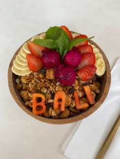 a bowl filled with fruit and nuts on top of a white table next to utensils