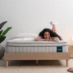 a woman laying on top of a bed in a room next to a potted plant