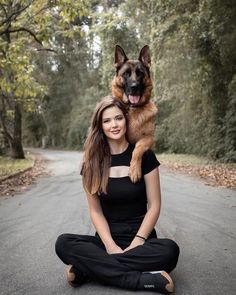 a woman sitting in the middle of a road with her dog on her shoulders and legs