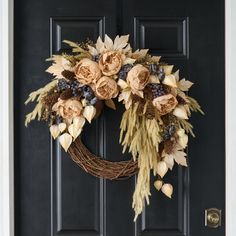 a wreath with dried flowers and leaves hanging on the front door to welcome people into the house