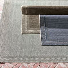 three different shades of blue and grey on a rug with brick flooring in the background