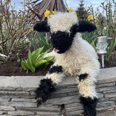 a stuffed sheep sitting on the side of a brick wall next to flowers and plants