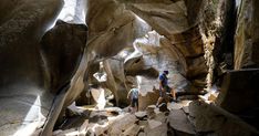 two people are walking through a narrow canyon in the mountains, with large rocks and boulders on either side