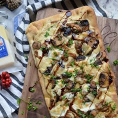 a pizza sitting on top of a wooden cutting board next to cheese and other food